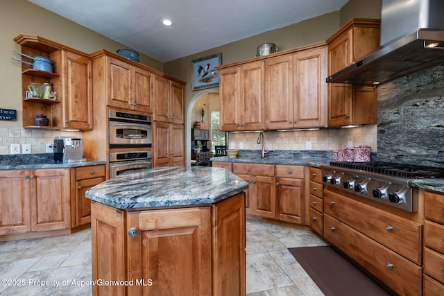 759 36 3/10 Rd, Palisade, CO 81526 - kitchen featuring wall chimney exhaust hood, appliances with stainless steel finishes, brown cabinets, decorative backsplash, and arched walkways