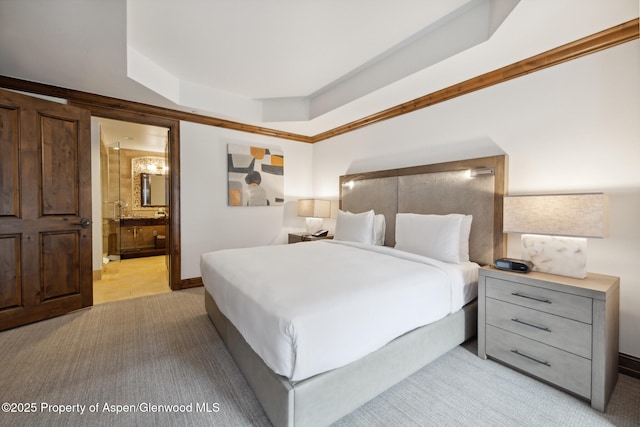 bedroom with a raised ceiling, connected bathroom, and light colored carpet