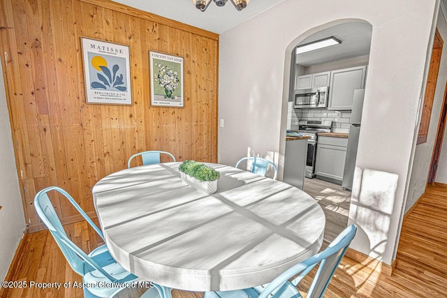 828 Taylor St, Craig, CO 81625 - dining room featuring arched walkways, wooden walls, and light wood-style flooring