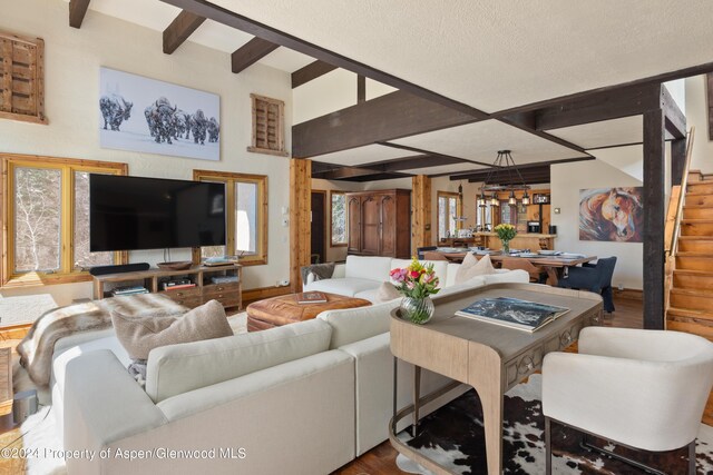 living room with beamed ceiling, wood-type flooring, and an inviting chandelier