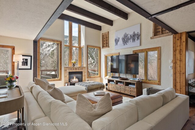 living room with beam ceiling, a textured ceiling, and a tiled fireplace