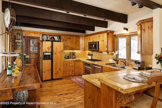 kitchen featuring sink, beamed ceiling, kitchen peninsula, light hardwood / wood-style floors, and appliances with stainless steel finishes