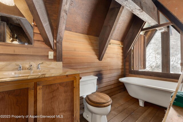 bathroom with wood walls, a bathing tub, sink, hardwood / wood-style flooring, and toilet