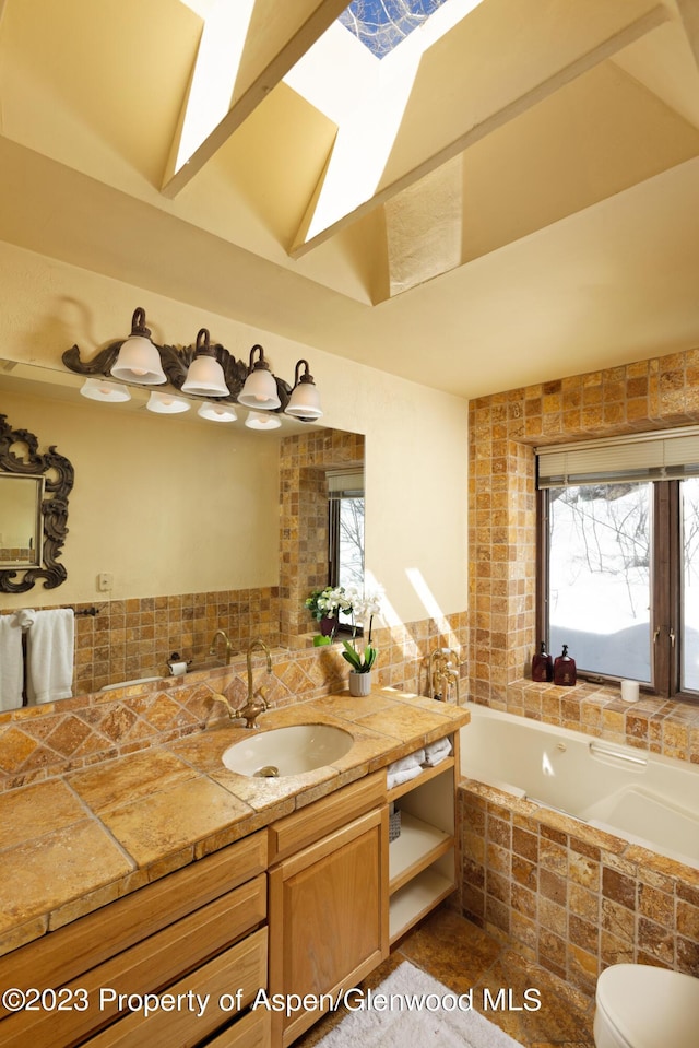 bathroom featuring vanity, a healthy amount of sunlight, tiled tub, and a skylight