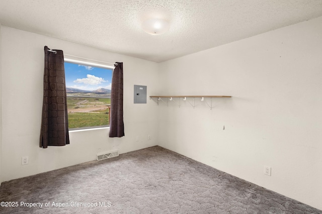 empty room with carpet flooring, a textured ceiling, visible vents, and electric panel