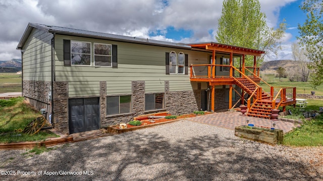 back of house featuring stone siding, a wooden deck, stairway, a patio area, and metal roof