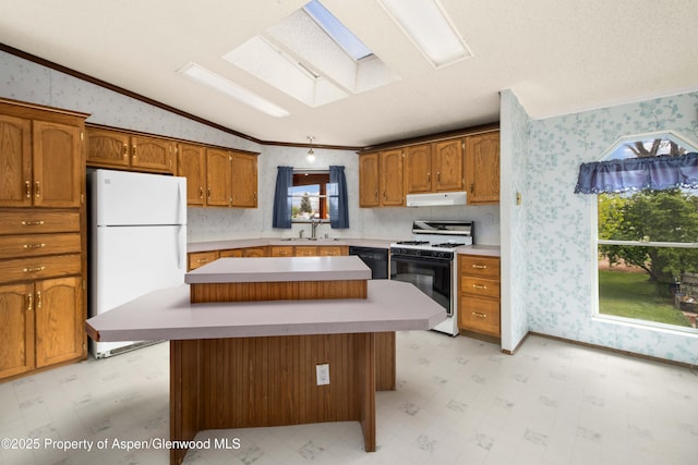 kitchen featuring crown molding, freestanding refrigerator, wallpapered walls, under cabinet range hood, and gas range oven