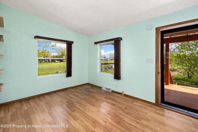 empty room featuring light wood-style floors, baseboards, and visible vents