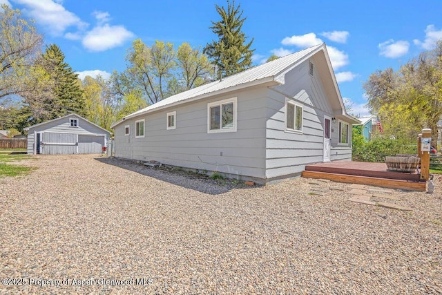 view of side of property with a garage, a deck, metal roof, and an outbuilding