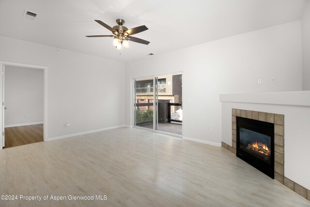 unfurnished living room with ceiling fan, light hardwood / wood-style floors, and a tiled fireplace