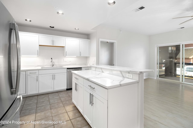 kitchen with white cabinets, sink, light stone counters, kitchen peninsula, and stainless steel appliances