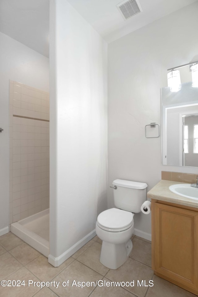 bathroom featuring tile patterned flooring, a tile shower, vanity, and toilet