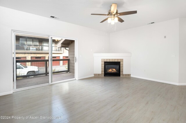 unfurnished living room with a tile fireplace, ceiling fan, and wood-type flooring