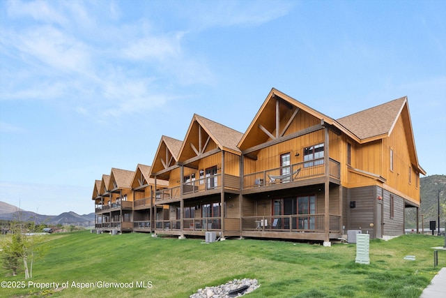 back of property with a balcony, a yard, a shingled roof, and board and batten siding