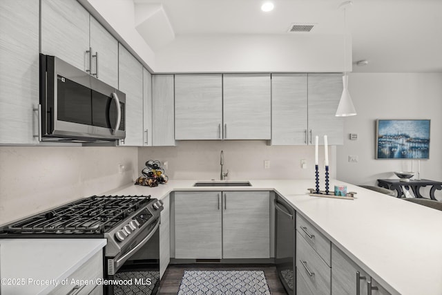 kitchen featuring appliances with stainless steel finishes, a sink, light countertops, dark wood-style flooring, and recessed lighting