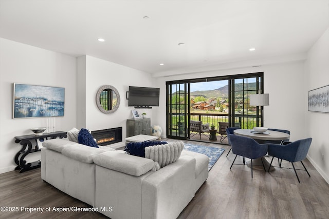 living room featuring wood finished floors, a glass covered fireplace, baseboards, and recessed lighting