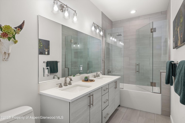 full bath featuring toilet, double vanity, and bath / shower combo with glass door