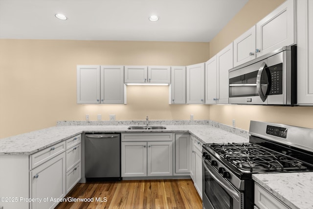 kitchen featuring light stone countertops, light wood-type flooring, a peninsula, stainless steel appliances, and a sink