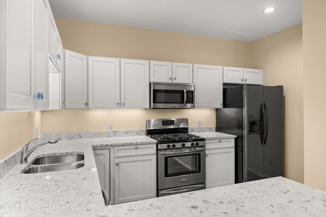 kitchen featuring light stone countertops, recessed lighting, a sink, appliances with stainless steel finishes, and white cabinetry