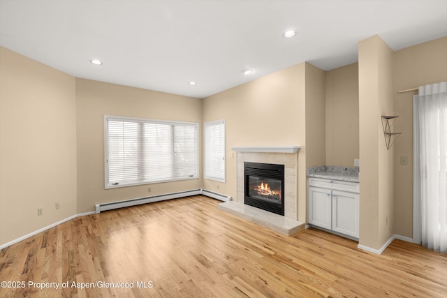 unfurnished living room with baseboard heating, recessed lighting, light wood-type flooring, and a glass covered fireplace