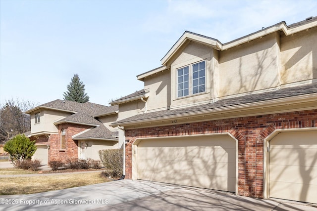 multi unit property featuring brick siding, stucco siding, an attached garage, and concrete driveway