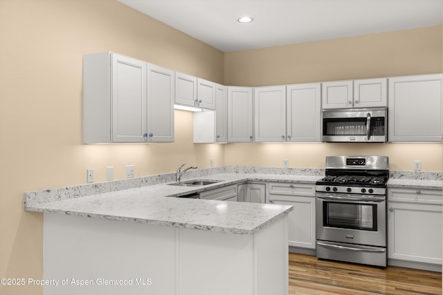 kitchen with light wood finished floors, a peninsula, white cabinets, stainless steel appliances, and a sink