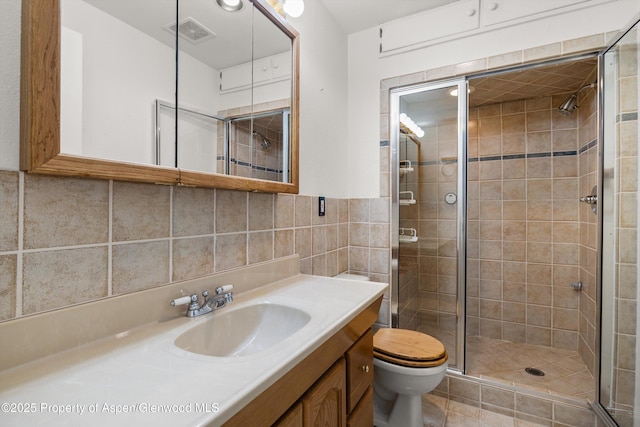 bathroom with visible vents, toilet, vanity, a stall shower, and tile walls