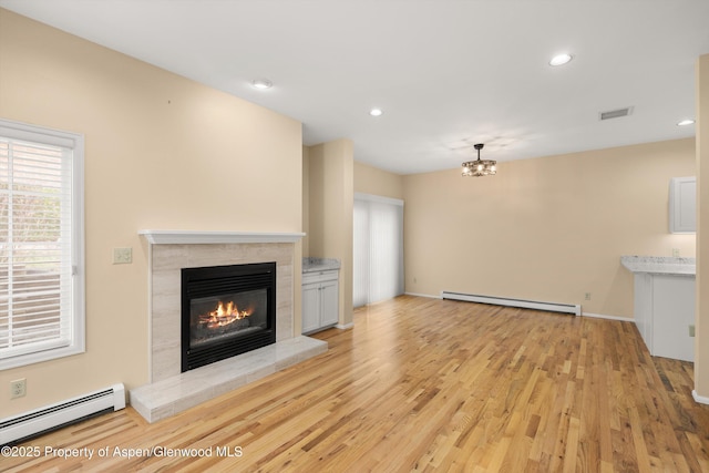 unfurnished living room featuring a tiled fireplace, light wood-type flooring, and baseboard heating