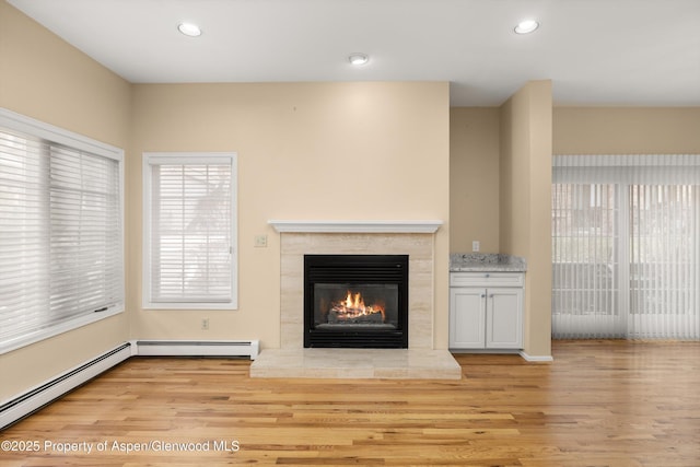 unfurnished living room with a premium fireplace, a baseboard heating unit, wood finished floors, and recessed lighting