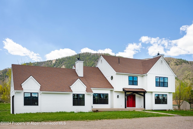 modern farmhouse featuring a chimney, a mountain view, a front lawn, and board and batten siding