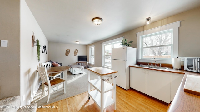 kitchen featuring plenty of natural light, white cabinets, light wood-style flooring, freestanding refrigerator, and a sink