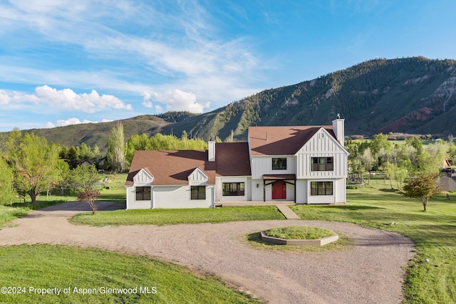 modern inspired farmhouse featuring driveway, a chimney, a mountain view, board and batten siding, and a front yard