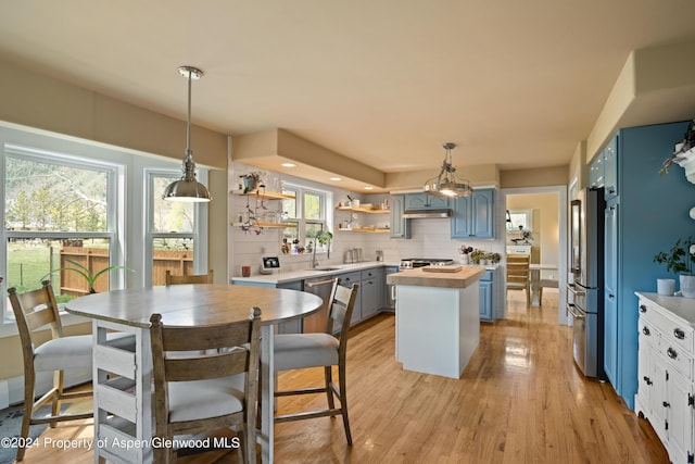 kitchen with light wood finished floors, tasteful backsplash, a center island, under cabinet range hood, and open shelves