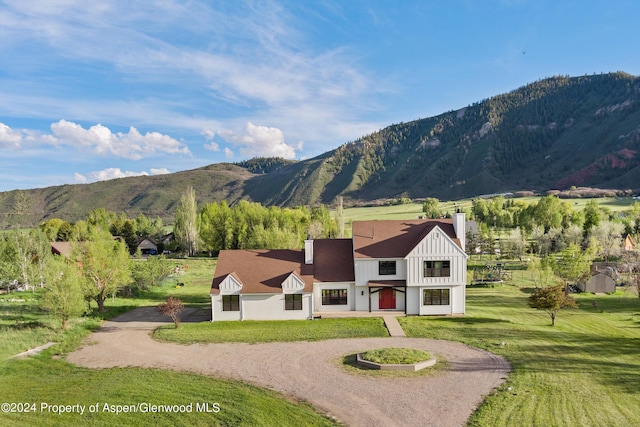 exterior space with driveway, a chimney, a mountain view, board and batten siding, and a front yard