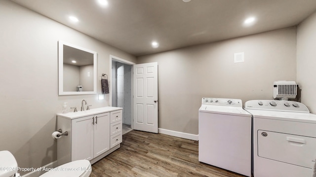 clothes washing area featuring laundry area, baseboards, wood finished floors, washer and dryer, and a sink