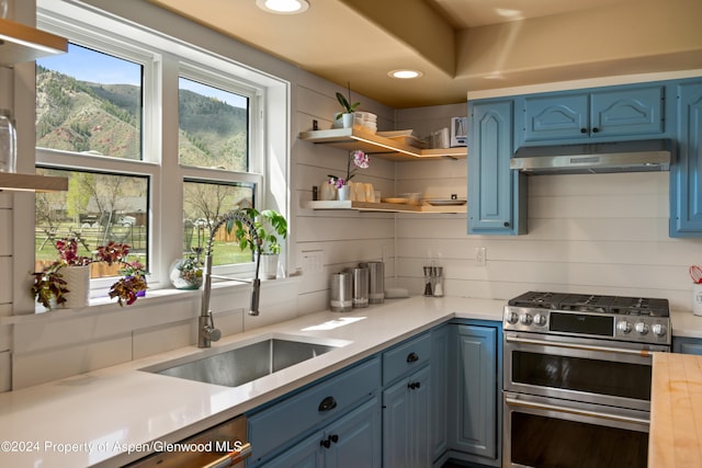 kitchen with range with two ovens, under cabinet range hood, a sink, light countertops, and blue cabinetry