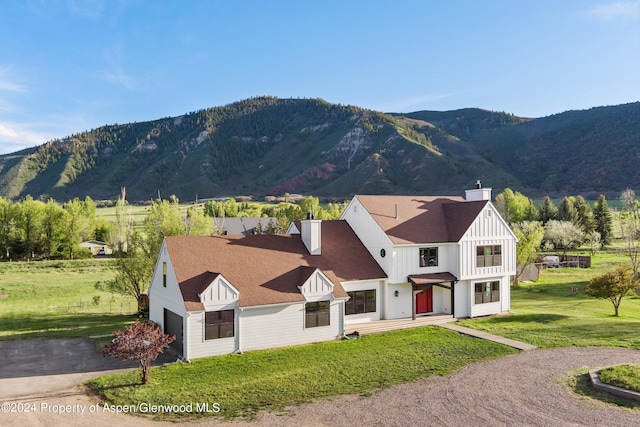 view of front of property with a mountain view, driveway, board and batten siding, a chimney, and a front yard