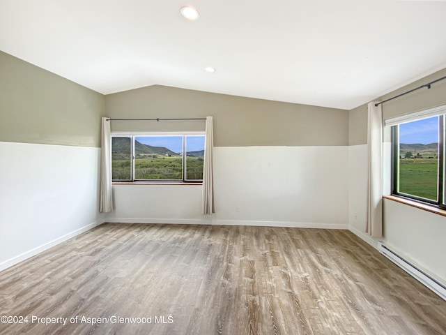 empty room with vaulted ceiling, light wood-type flooring, and a baseboard heating unit