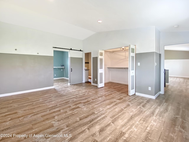 interior space with light wood-type flooring, a barn door, a spacious closet, and lofted ceiling