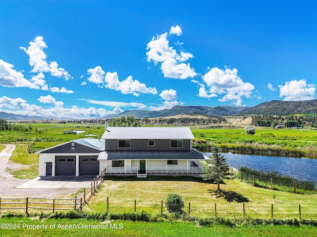 view of front of home featuring a water and mountain view, a rural view, a front lawn, covered porch, and a garage