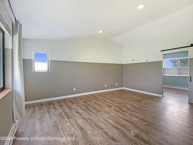 empty room with wood-type flooring, a baseboard radiator, and lofted ceiling