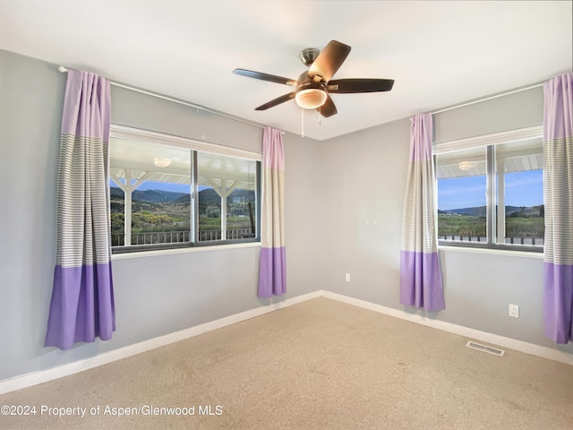 empty room featuring a mountain view, carpet flooring, and ceiling fan