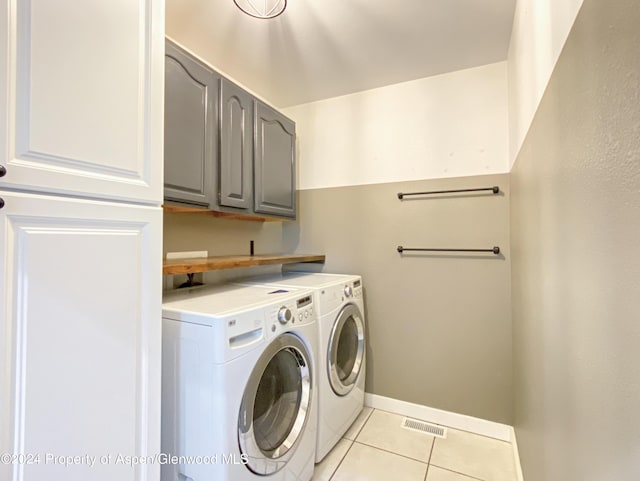 clothes washing area with separate washer and dryer, light tile patterned floors, and cabinets