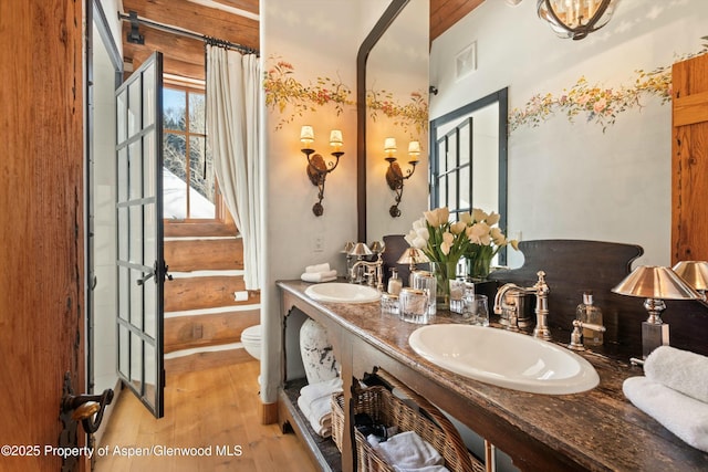 bathroom featuring wood-type flooring, vanity, rustic walls, and toilet