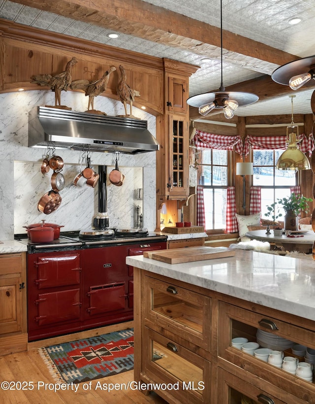 kitchen with pendant lighting, range hood, beamed ceiling, light stone counters, and light wood-type flooring