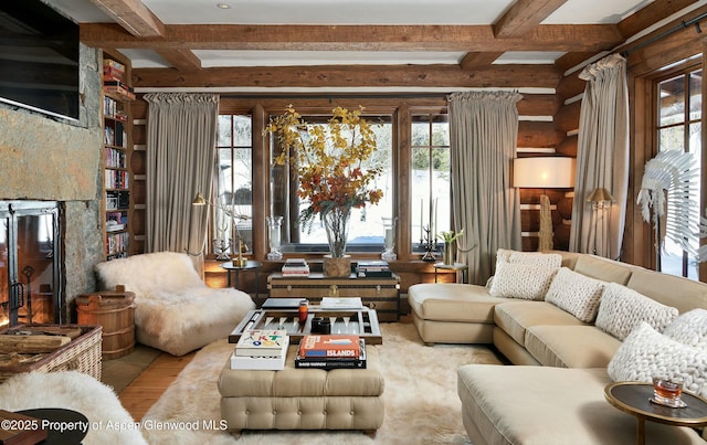 living room featuring beam ceiling, a stone fireplace, and rustic walls