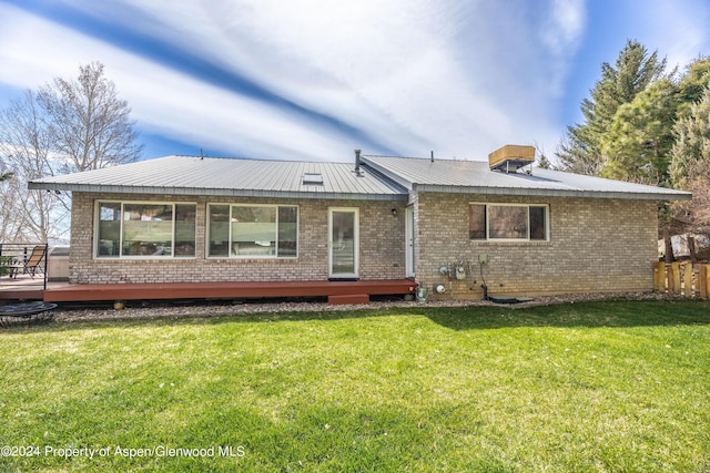 rear view of house featuring brick siding, a deck, a yard, and metal roof