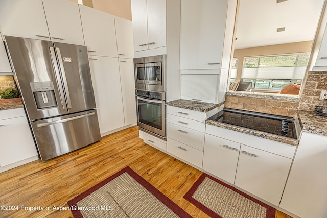 kitchen featuring stainless steel appliances, light wood-type flooring, white cabinetry, stone counters, and backsplash