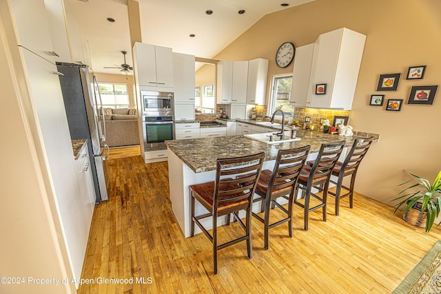 kitchen featuring stainless steel appliances, a peninsula, light wood-style floors, a kitchen bar, and high vaulted ceiling