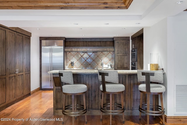 kitchen featuring a kitchen breakfast bar, stainless steel built in fridge, tasteful backsplash, and light hardwood / wood-style flooring